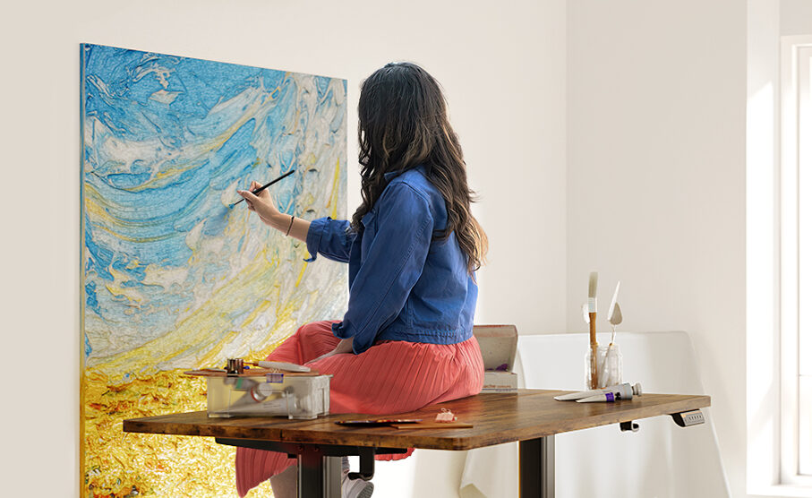 Ergonomic desks sat on by a woman painting on a canvas on the wall